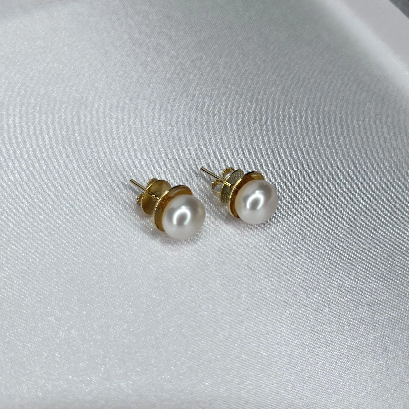Pearl stud earrings in recycled gold on white satin